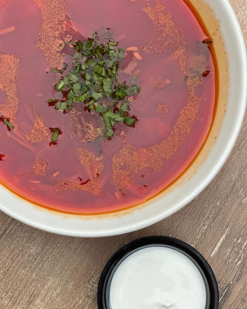 A bowl of borscht with herbs, seen from above, with a pot of sour cream