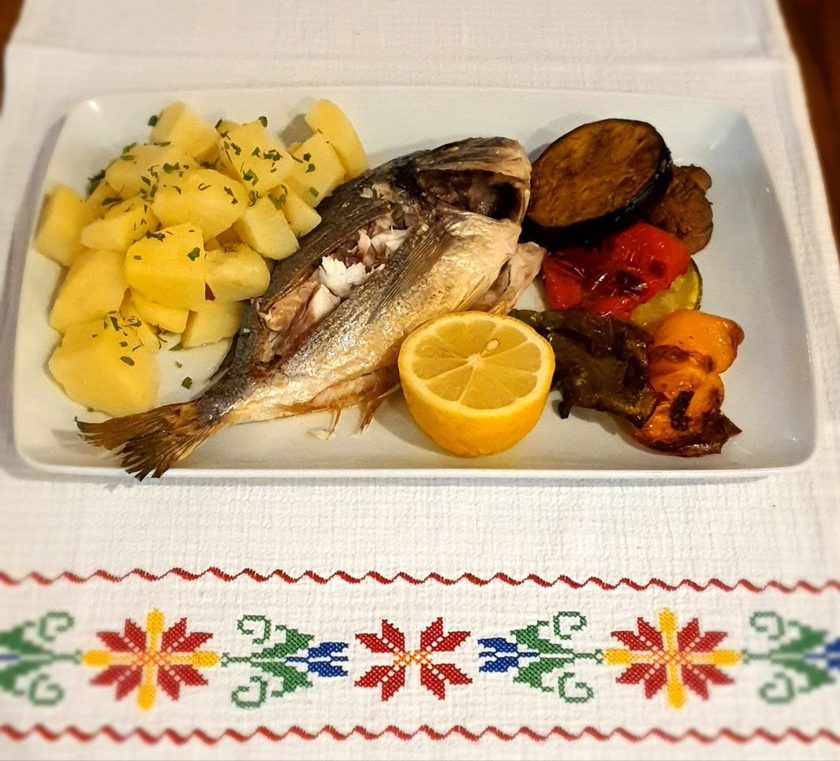 Grilled sea bream with boiled potatoes, grilled vegetables and lemon on an embroidered tablecloth