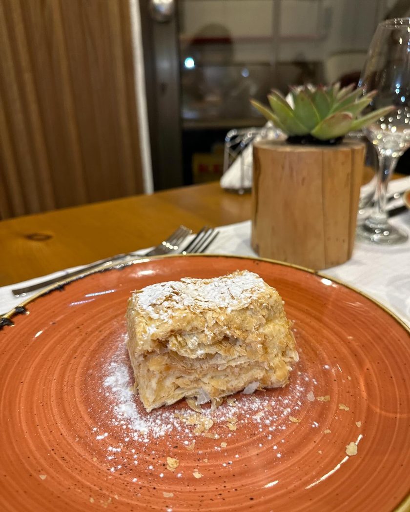 A slice of Napoleon cake dusted with sugar on an orange plate