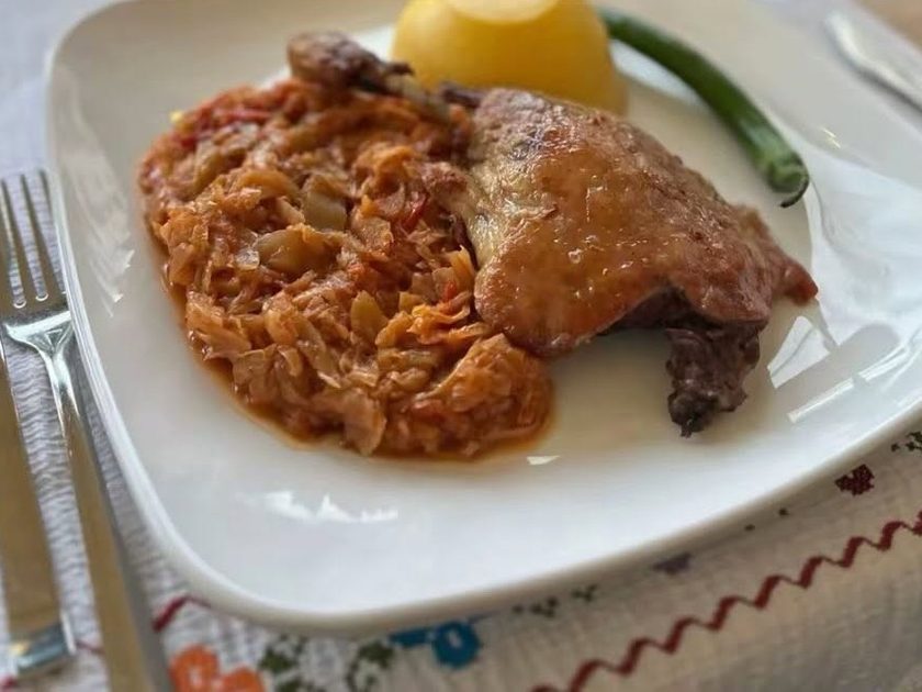 A roast duck leg on stewed cabbage with polenta and a green chilli on a white plate