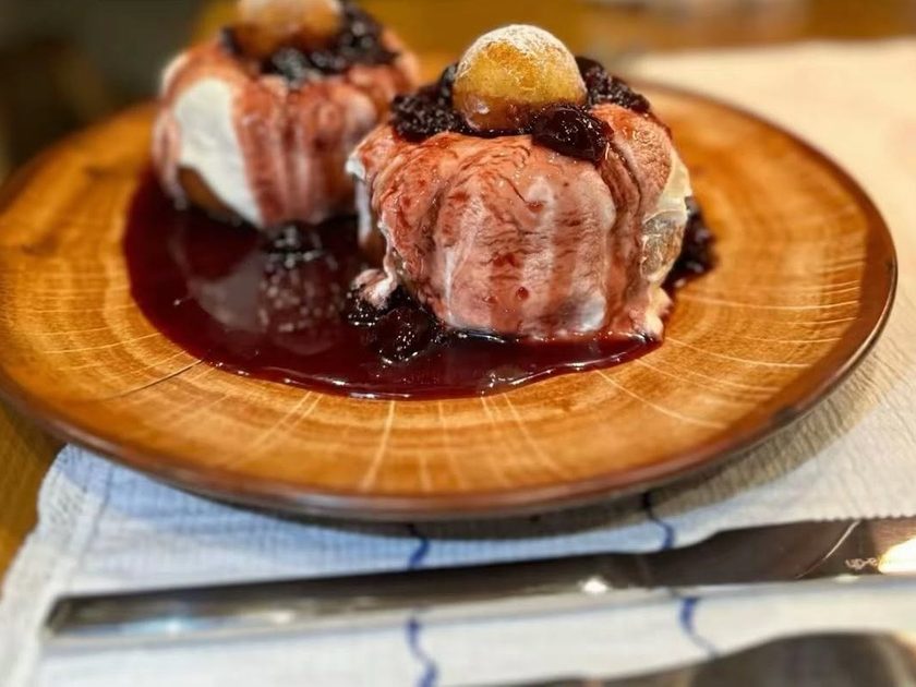 Two papanasi doughnuts under sour cream and sour cherry jam on a wooden plate