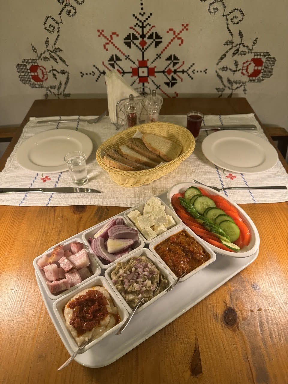 The traditional platter of lard, smoked pork, dips, cheese and vegetables with a bread basket, under a wall painted with red and black cross-stitch